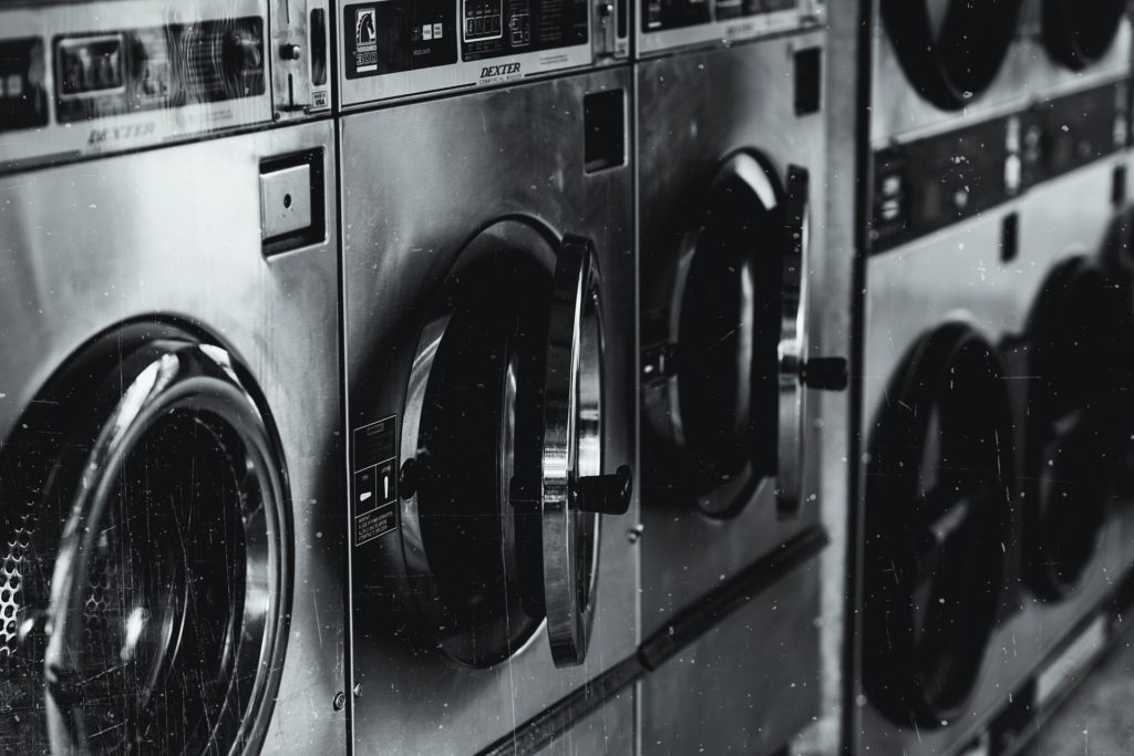 Mehrere Wärmepumpentrockner stehen in einem Waschsalon nebeneinander. Das Bild ist schwarz-weiß.